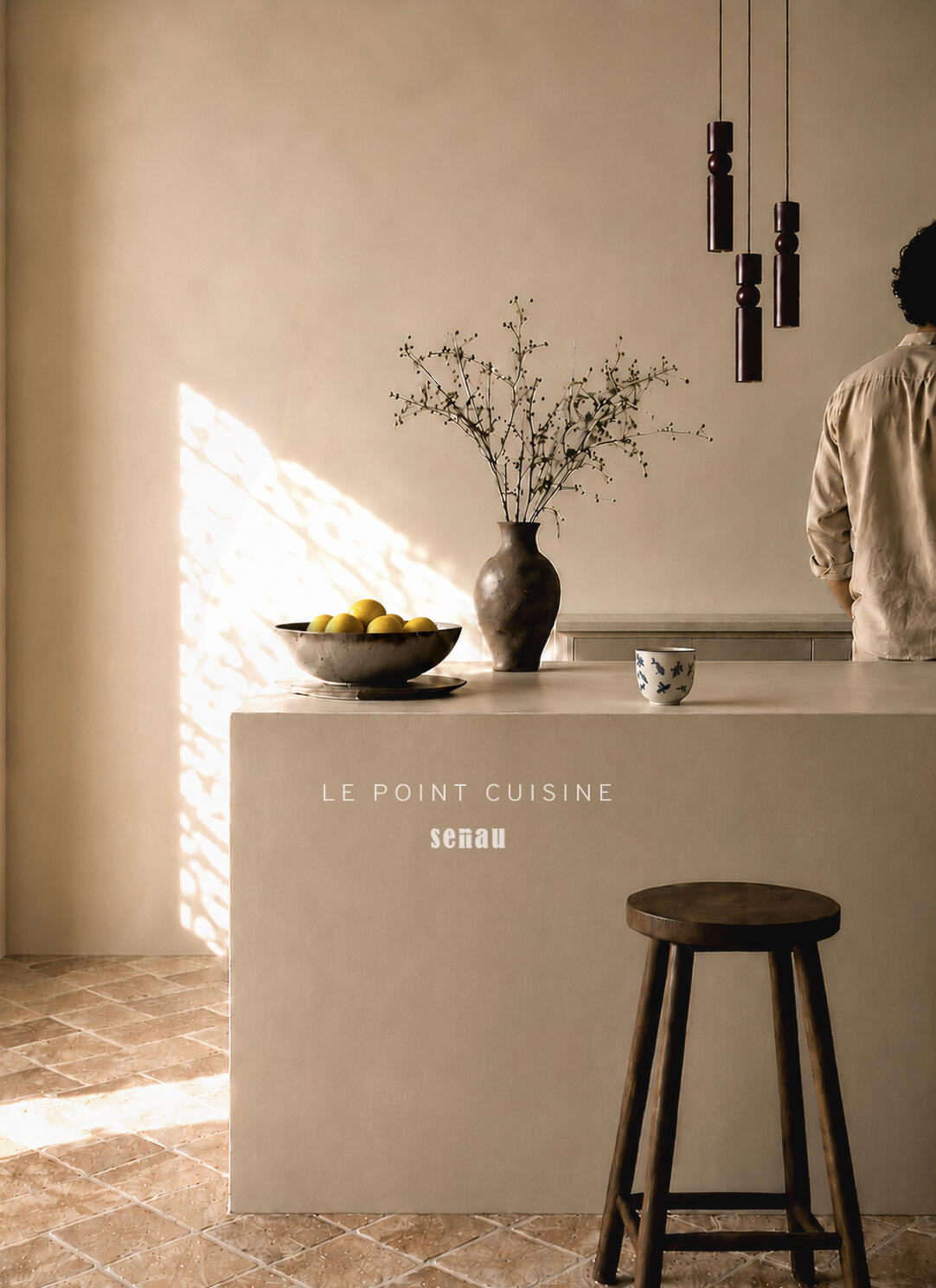 Ilot de cuisine en béton ciré baigné de lumière naturelle, sol tomette et suspension en bois foncé. Aix-en-Provence